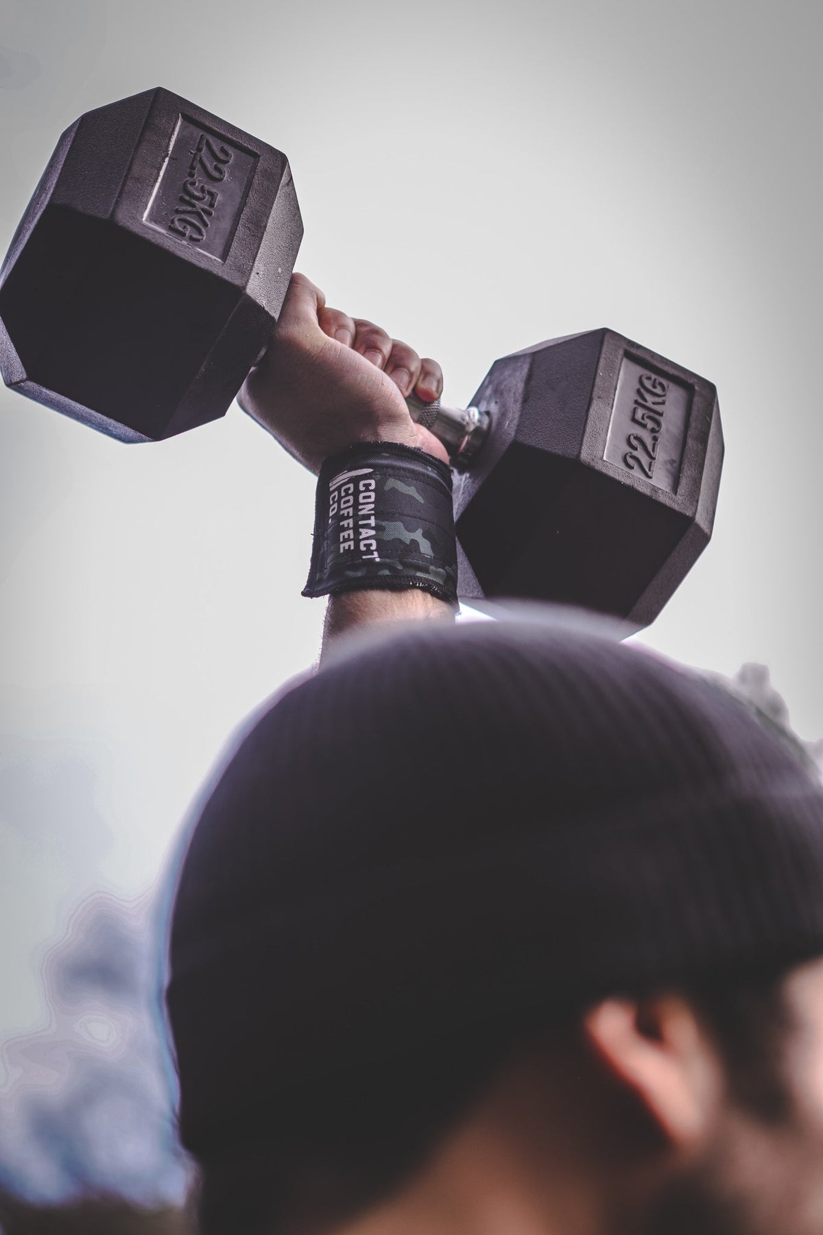 Camo wrist wraps with Contact Coffee Co. logo on wrists, holding dumbbells