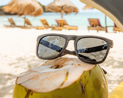 Polarised sunglasses with dark lenses on a beach, brown woodgrain-style frame