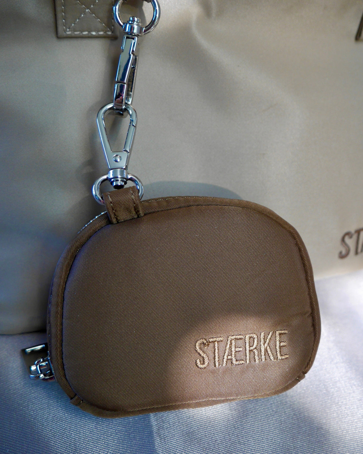 Espresso-brown round zip jewelry pouch with silver keyring clasp and gold logo text
