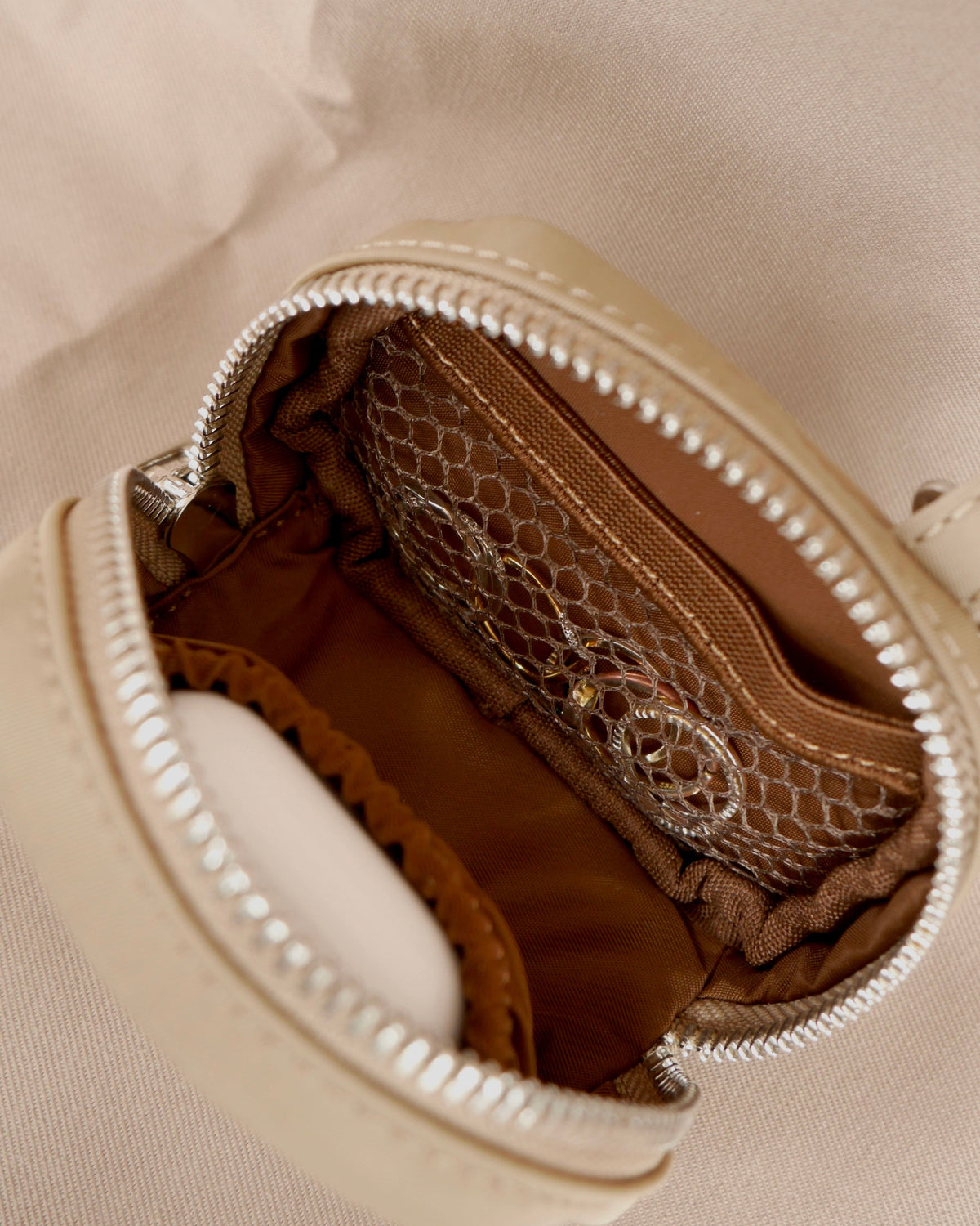 Sand-colored zip jewelry pouch opened, showing patterned inner lining and silver zipper