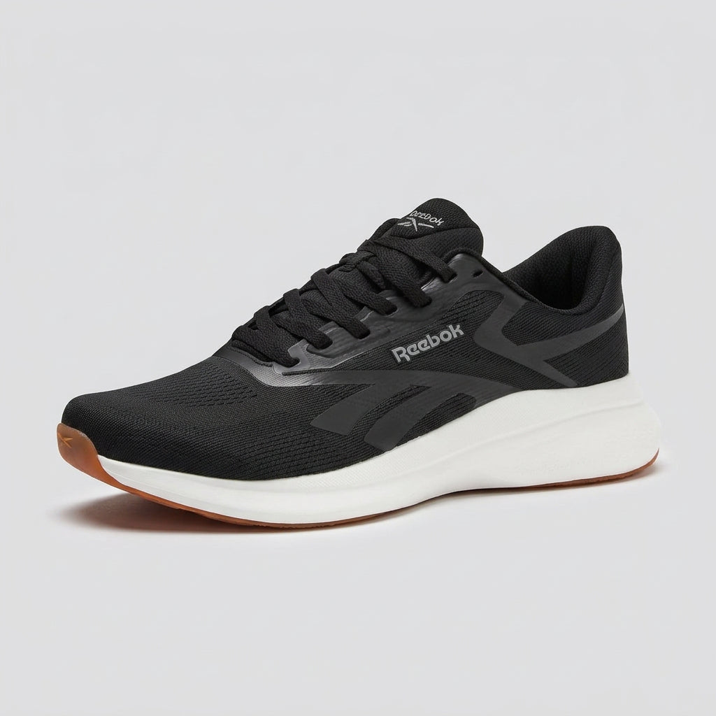 A Reebok athletic sneaker in black and dark gray with a thick white midsole and a gum brown outsole, shown from a three-quarters angle on a white background.
