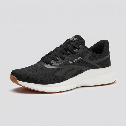 A Reebok athletic sneaker in black and dark gray with a thick white midsole and a gum brown outsole, shown from a three-quarters angle on a white background.