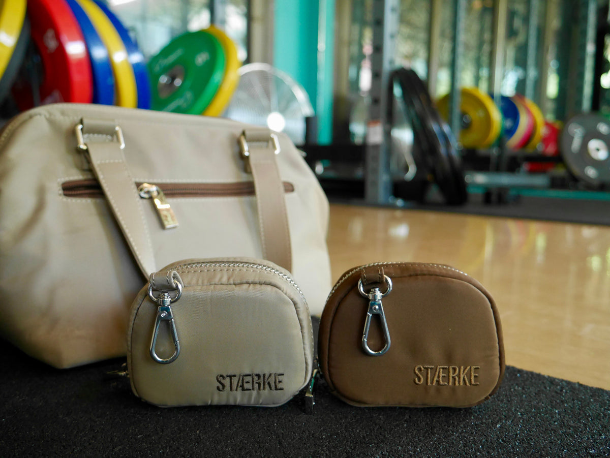 Small zip jewelry pouches, one sand and one espresso, with silver hooks and logo text