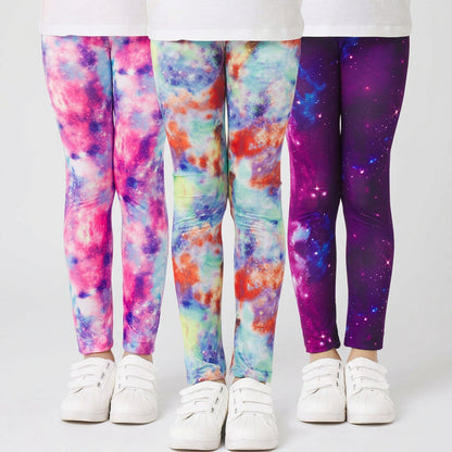 Three pairs of kids' leggings with vibrant tie-dye and galaxy prints, shown on models from the waist down wearing white sneakers against a white background.