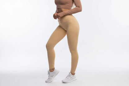 Person wearing beige leggings and a brown long-sleeve top on a white background