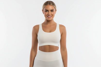 Woman wearing a white sports bra and leggings on a light gray background