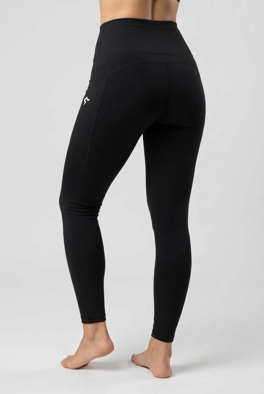Black high-waisted leggings with a small white logo on the left hip, shown on a model from a rear three-quarter angle against a light beige background.