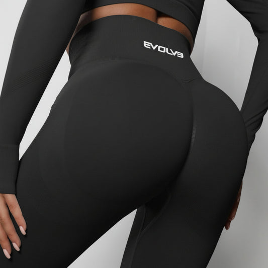 Person wearing black athletic leggings with 'Evolva' branding on a gray background