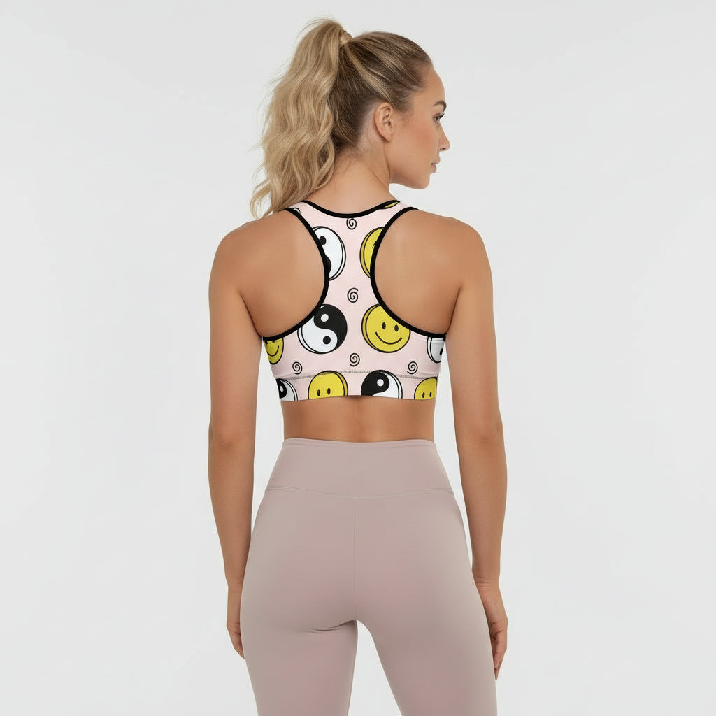 Woman wearing a sports bra with smiley face and yin yang design on a plain background