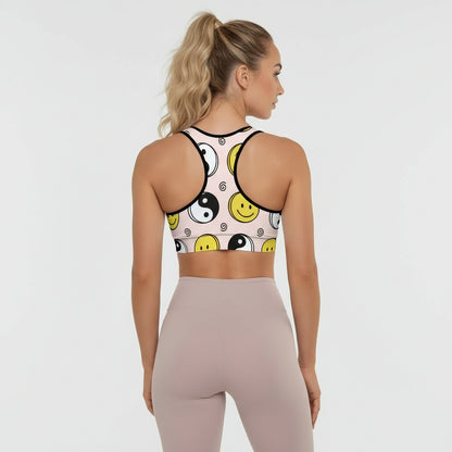 Woman wearing a sports bra with smiley face and yin yang design on a plain background