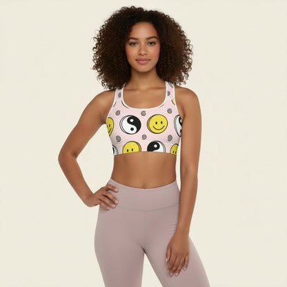 Woman wearing a sports bra with smiley face and yin yang design on a beige background