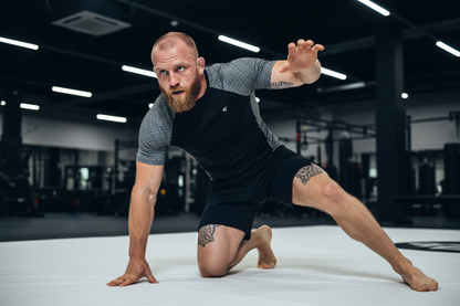 Man in athletic wear performing a yoga pose on a white mat in a gym.