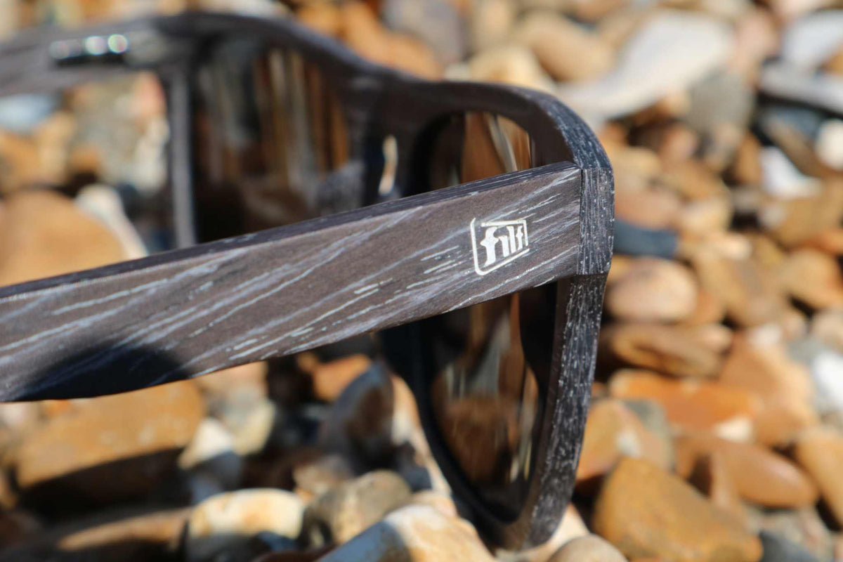 Polarised sunglasses temple close-up, brown frame with dark lens reflecting light