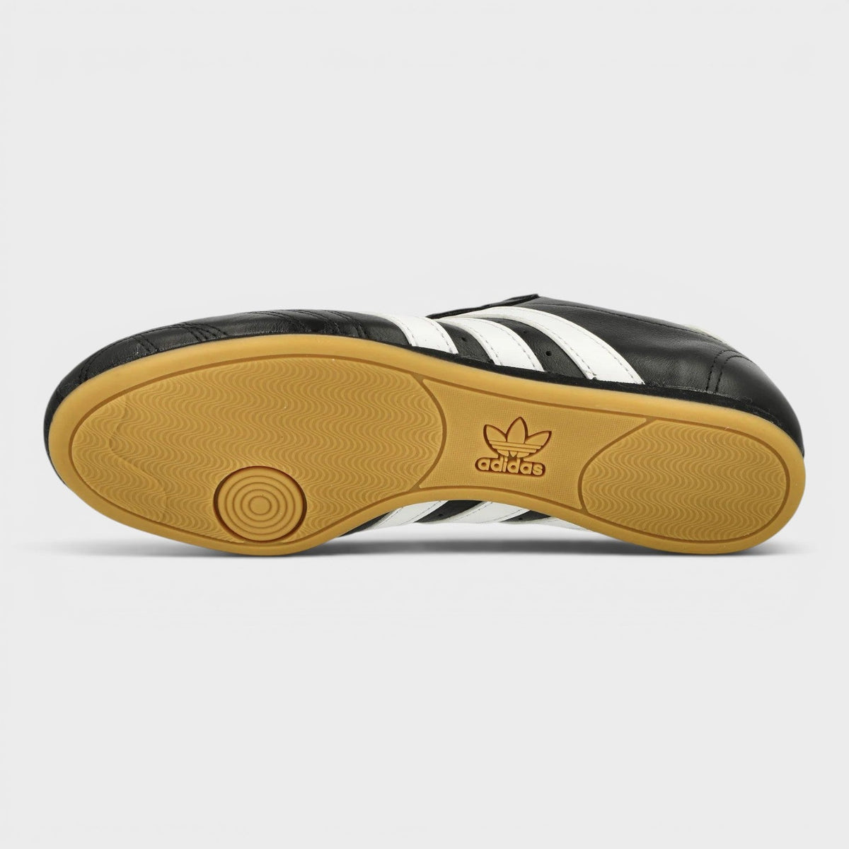 Black taekwondo shoes with white stripes and adidas logo on gum outsole