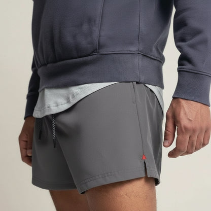 Person wearing gray shorts and a dark blue jacket on a beige background