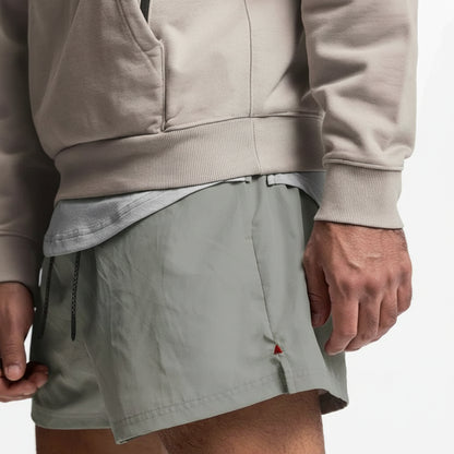 Person wearing a beige hoodie and gray shorts on a plain background