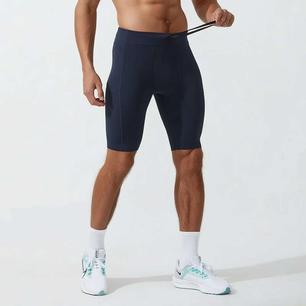 A man wearing navy Quick Dry Compression Shorts with an elastic waist, standing and facing away from the camera. He is also wearing white sneakers.