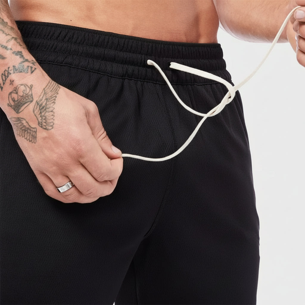 Person wearing black shorts holding a white cord, with tattoos on arm and ring on finger.