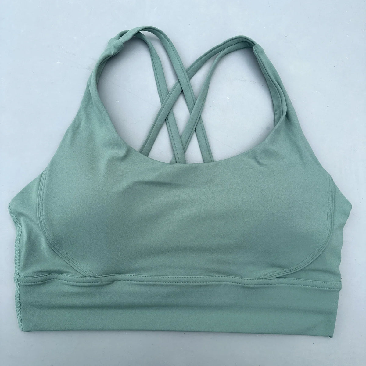 Sage green padded sports bra with crisscross cross-back straps and smooth elastic hem.