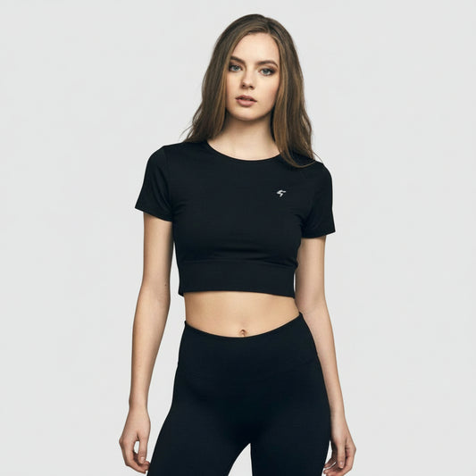 A woman wearing a black slim-fit crop tee with short sleeves, standing in front of a brick wall. The tee appears to be made of a soft and durable fabric.