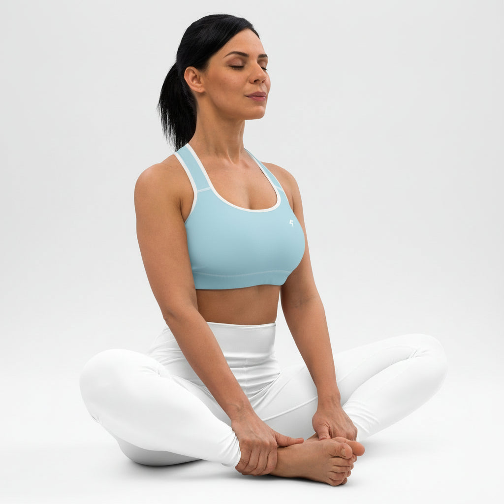 Woman in a light blue sports bra and white pants sitting with her legs crossed on a plain background