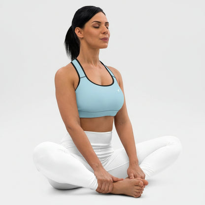 Woman in a light blue sports bra and white pants sitting cross-legged on a light gray background