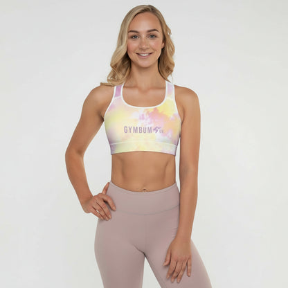 A woman wearing a multicolored tie-dye padded sports bra with a scoop neckline and shoulder straps, standing in a kneeling position with a smile on her face.