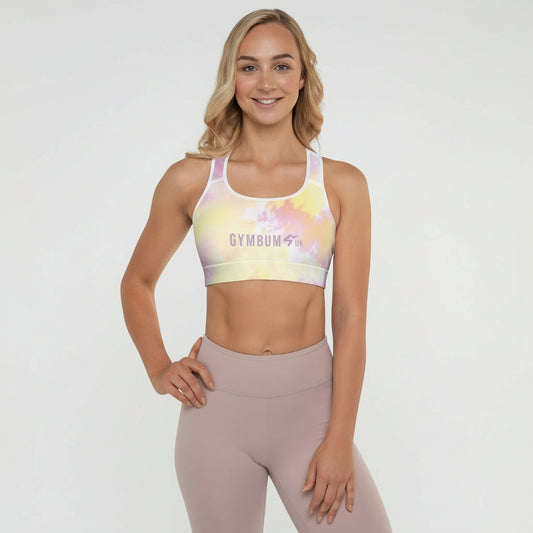 A woman wearing a multicolored tie-dye padded sports bra with a scoop neckline and shoulder straps, standing in a kneeling position with a smile on her face.