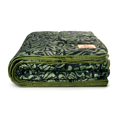 Folded camping blanket with green and dark leaf-pattern fabric and orange logo label