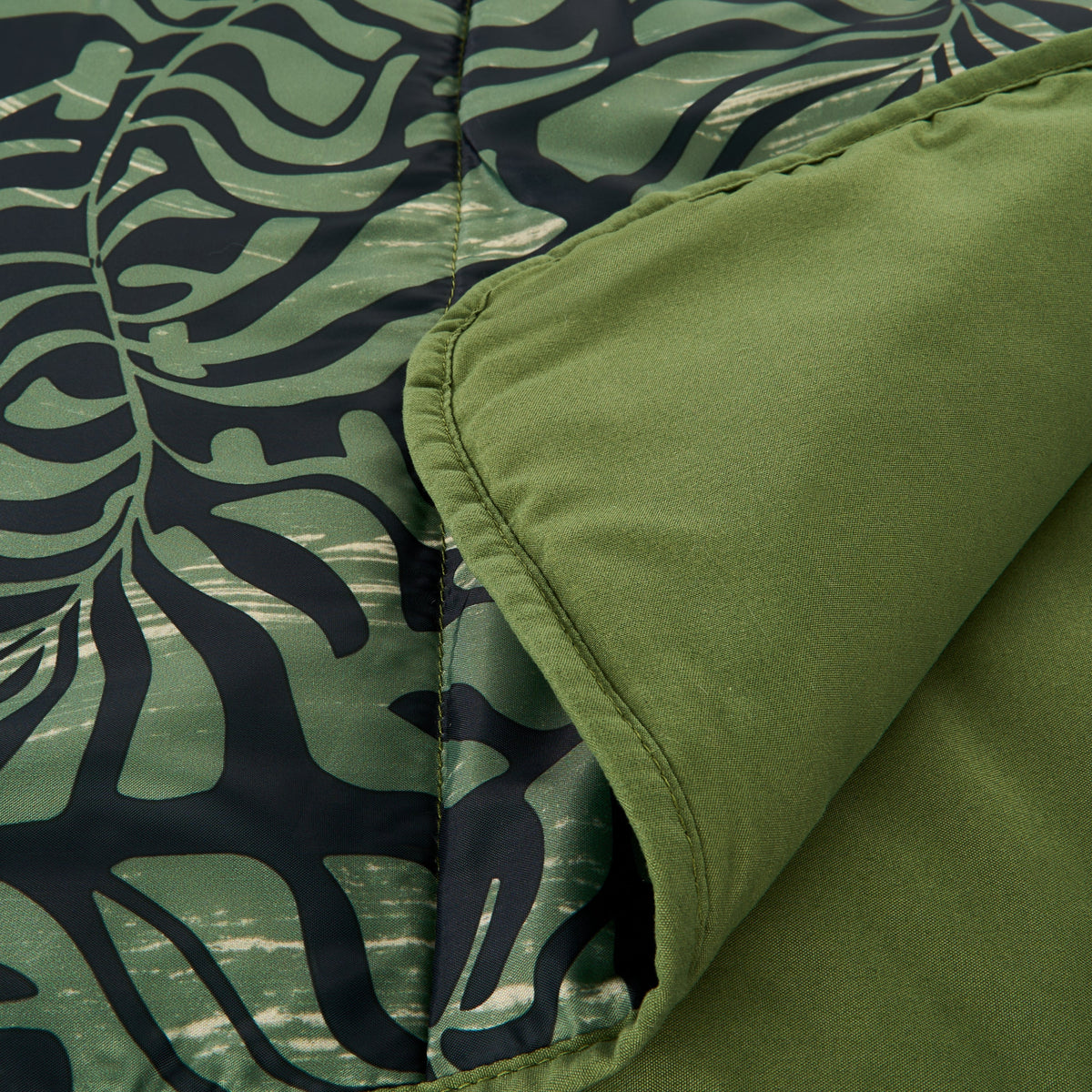 Close-up of dark teal and green leaf-pattern camping blanket with stitched edge