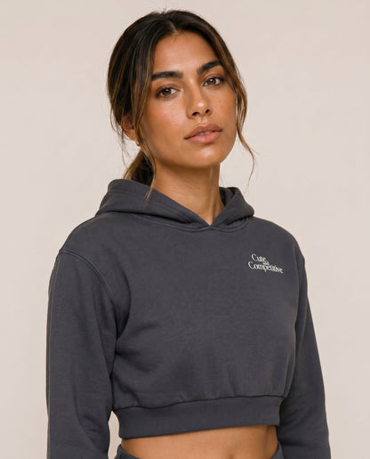 Charcoal gray cropped hoodie with hood and small chest logo, close-up.
