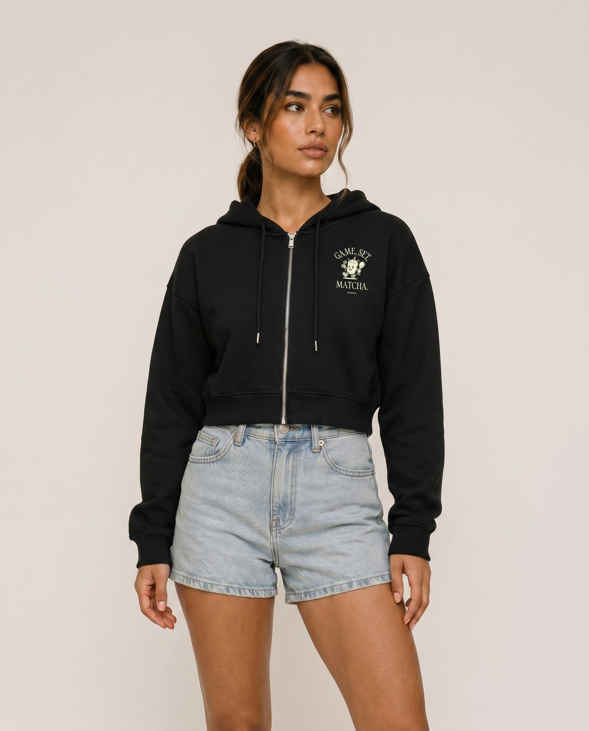 Black cropped zip hoodie with hood drawstrings and chest logo.