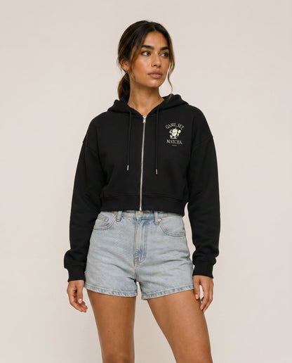 Black cropped zip hoodie with hood drawstrings and chest logo.