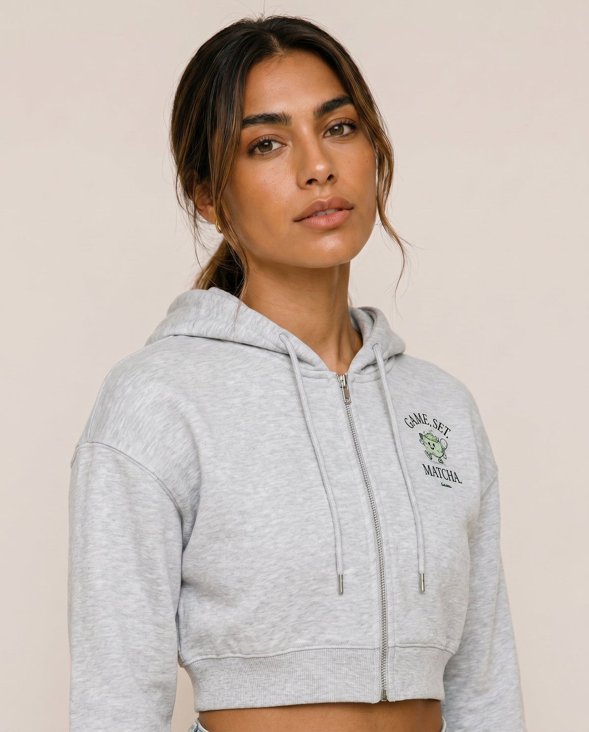 Light gray cropped zip hoodie with hood drawstrings and front logo print.