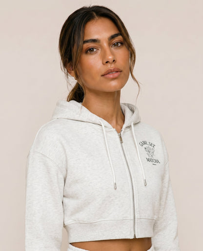 Light gray cropped zip hoodie close-up with hood drawstrings and front logo.