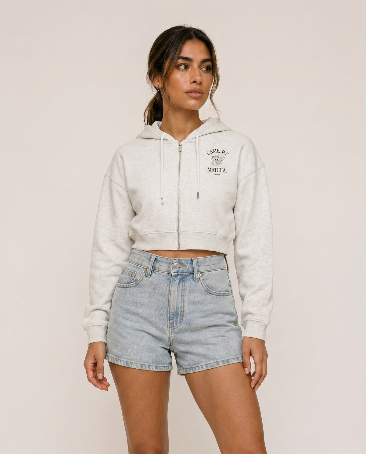 Front view of cropped zip hoodie in light gray with hood, drawstring, and chest print