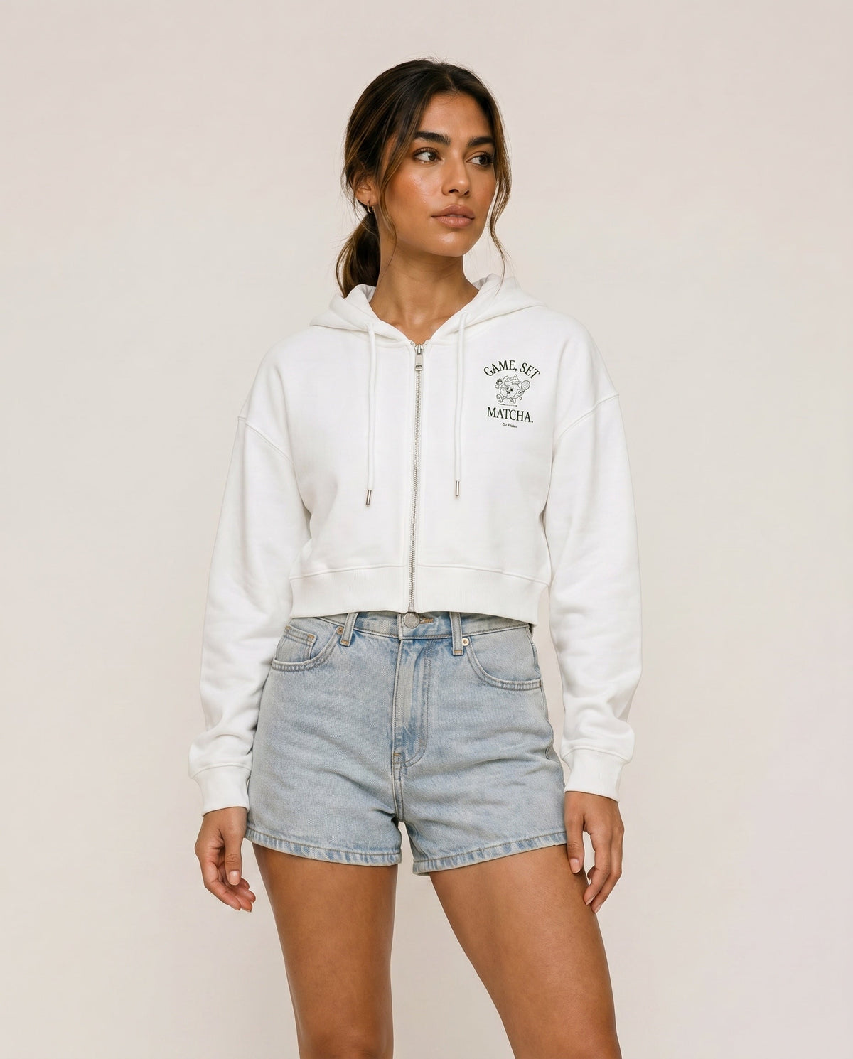 Front view of cropped zip hoodie in white with hood, drawstring, and chest print