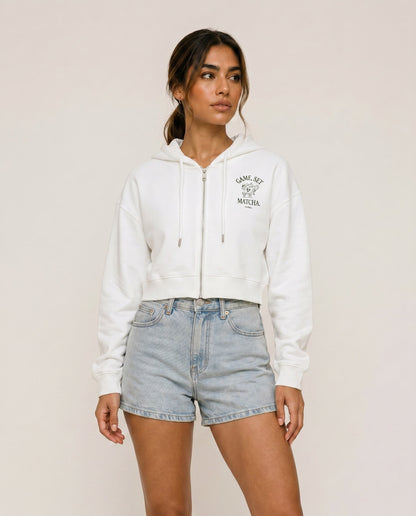 Front view of cropped zip hoodie in white with hood, drawstring, and chest print