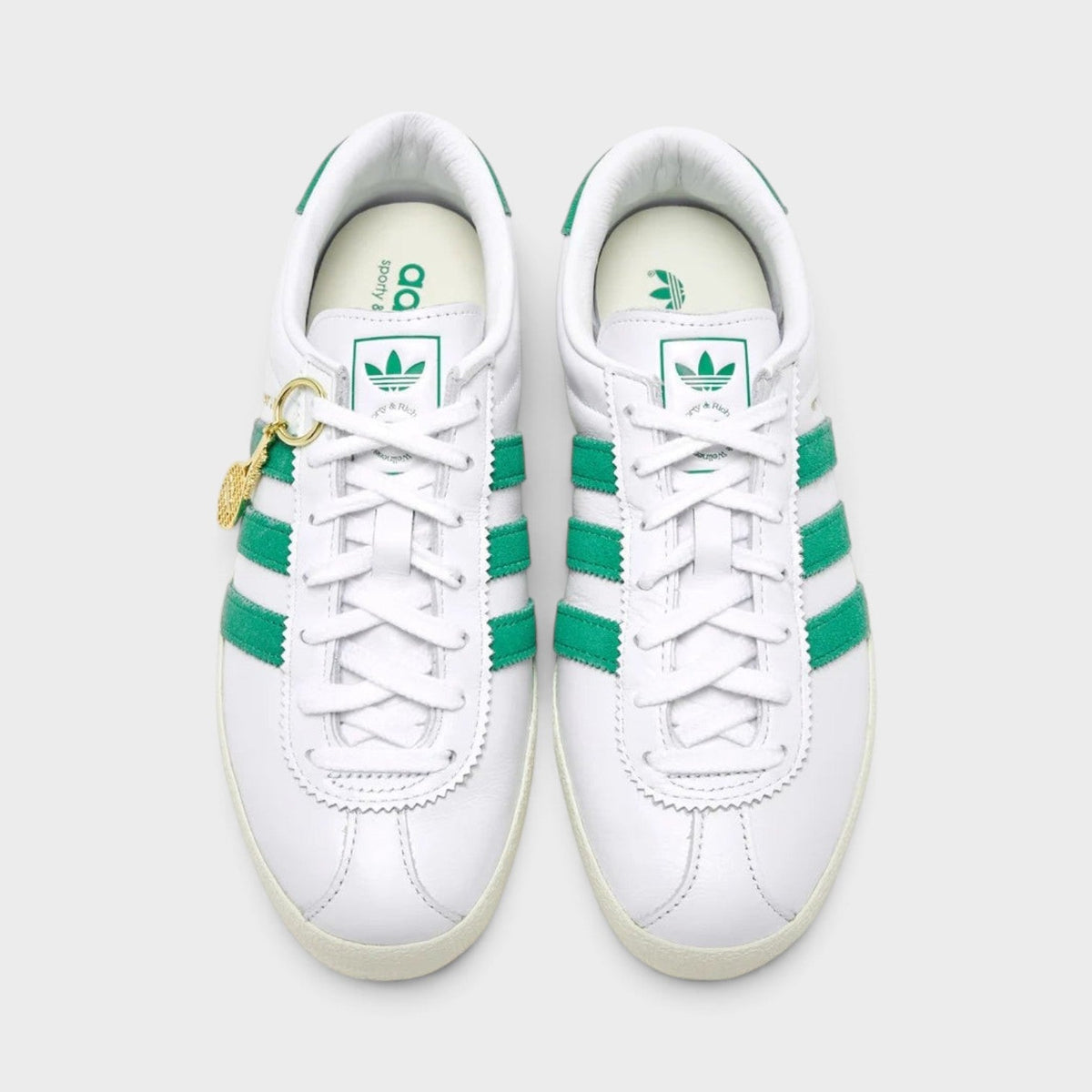 Pair of white lace-up sneakers with green stripe detailing and gold lace charm