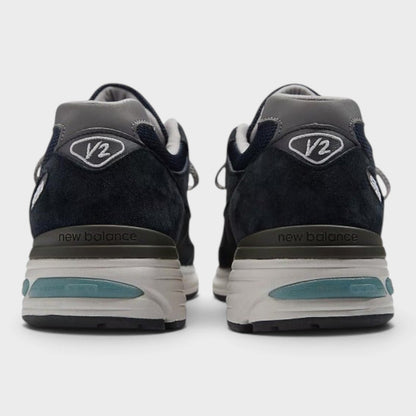Dark navy New Balance 991v2 sneakers with heel tab, V2 branding, and teal stripe