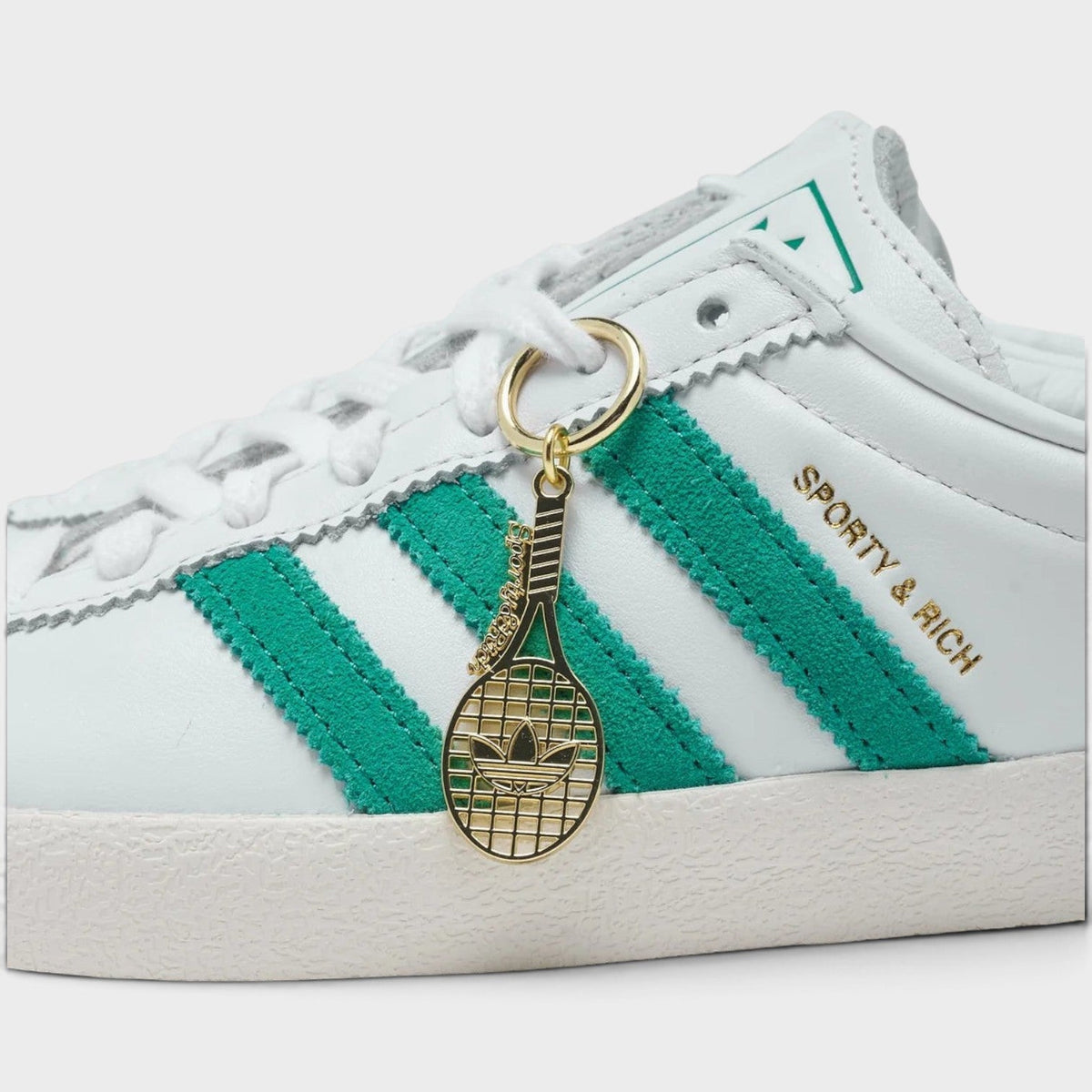 White sneaker side close-up with green stripes, gold keychain charm, 'SPORTY RICH'