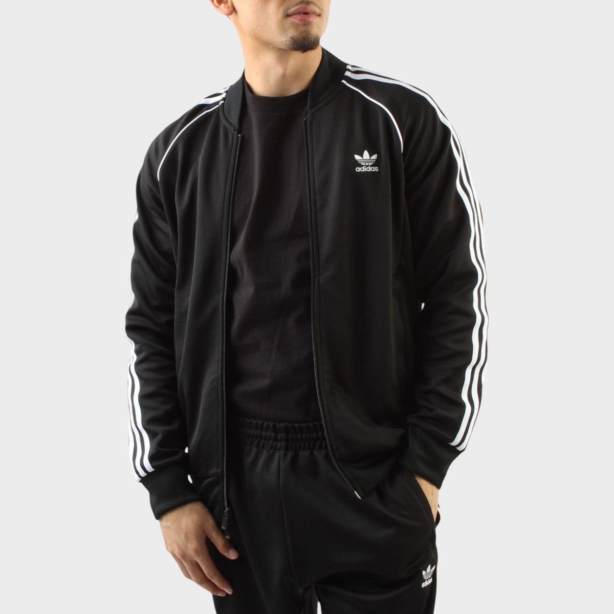 Black track jacket with white triple stripe sleeves, full-zip front, and trefoil logo