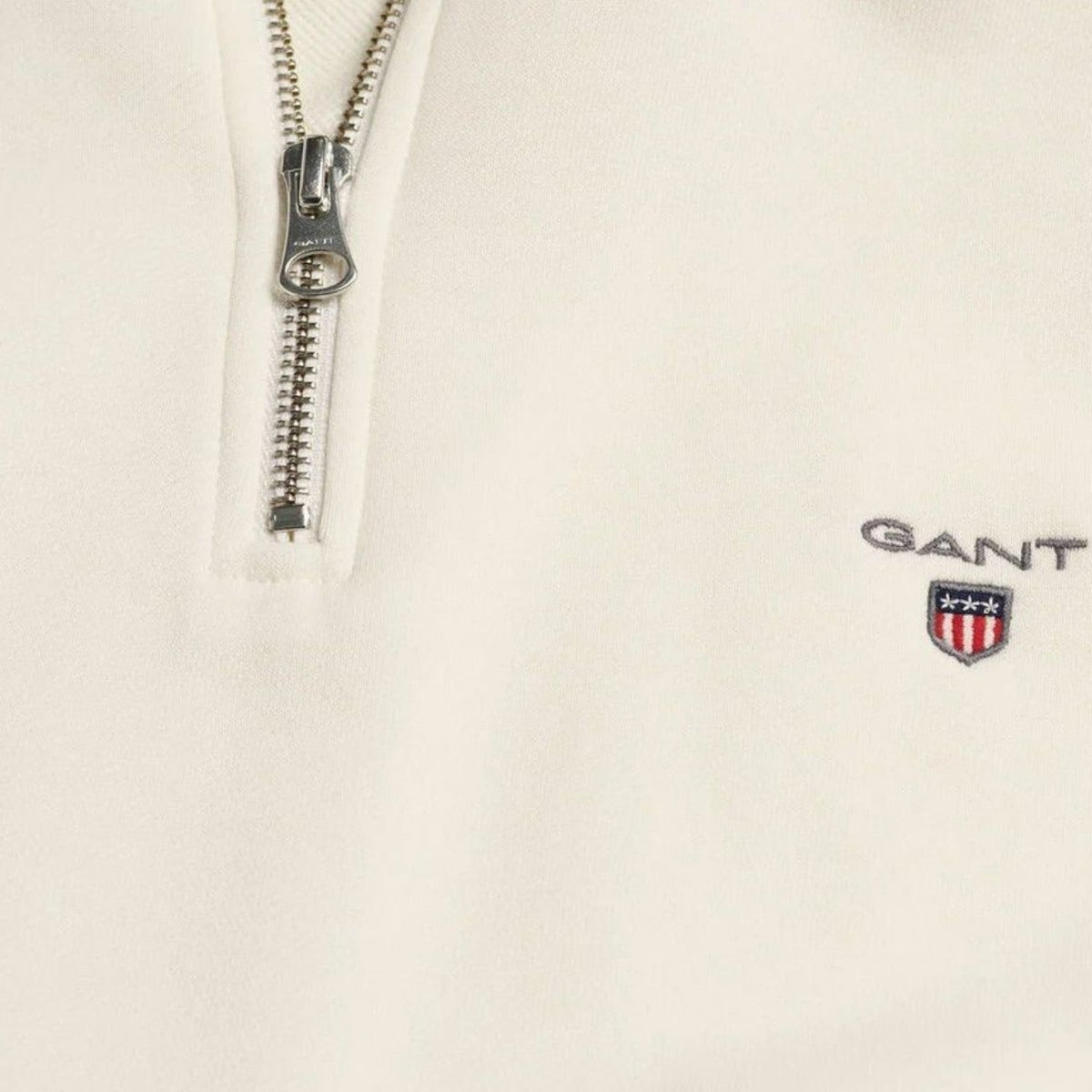Cream half-zip sweater close-up: silver zipper and chest logo patch