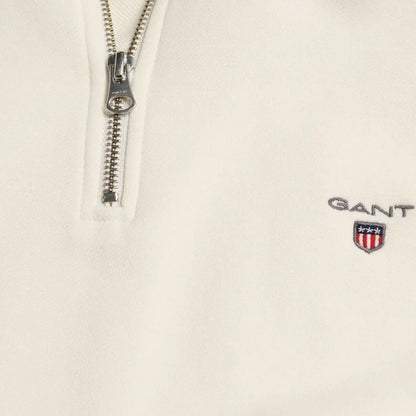 Cream half-zip sweater close-up: silver zipper and chest logo patch