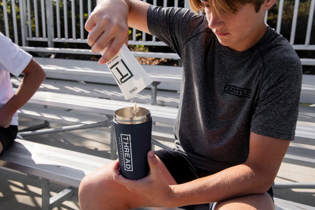 Protein powder sachet pouring into shaker cup outdoors; white packet held above cup.