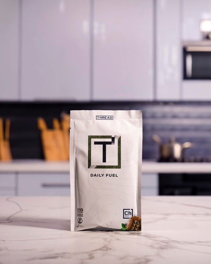 Daily Fuel protein powder pouch standing on marble surface, white bag with green T logo.
